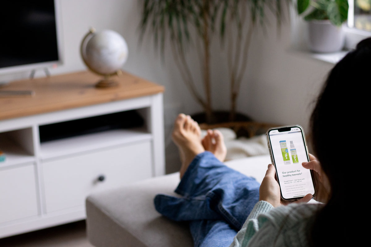 Person browsing FunghiClear® foot care products on a smartphone while resting at home